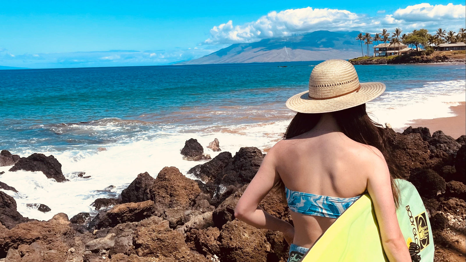 Female model wearing Hana Palm Sun Hat, showcasing the wide brim and palm straw weave on the way to surf.