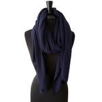 A navy blue textured infinity scarf draped on a black mannequin torso against a textured off-white wall.