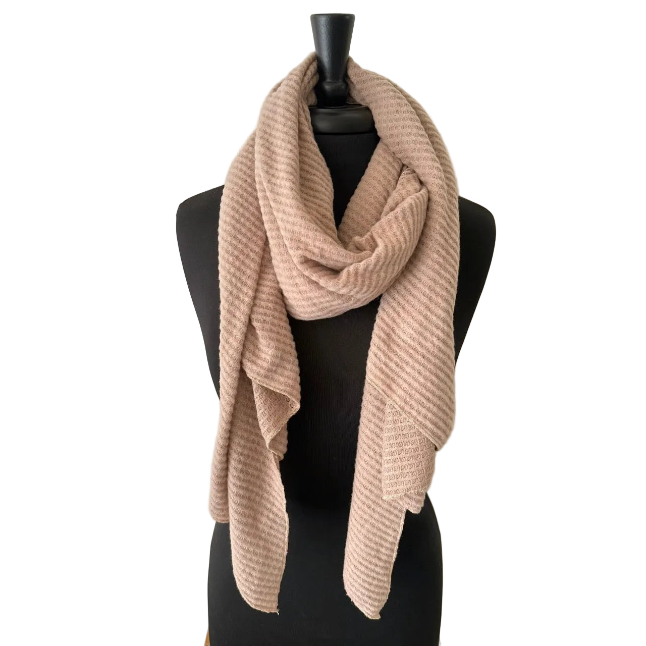 A light blush pink ribbed knit scarf draped on a black mannequin torso against a textured off-white wall.