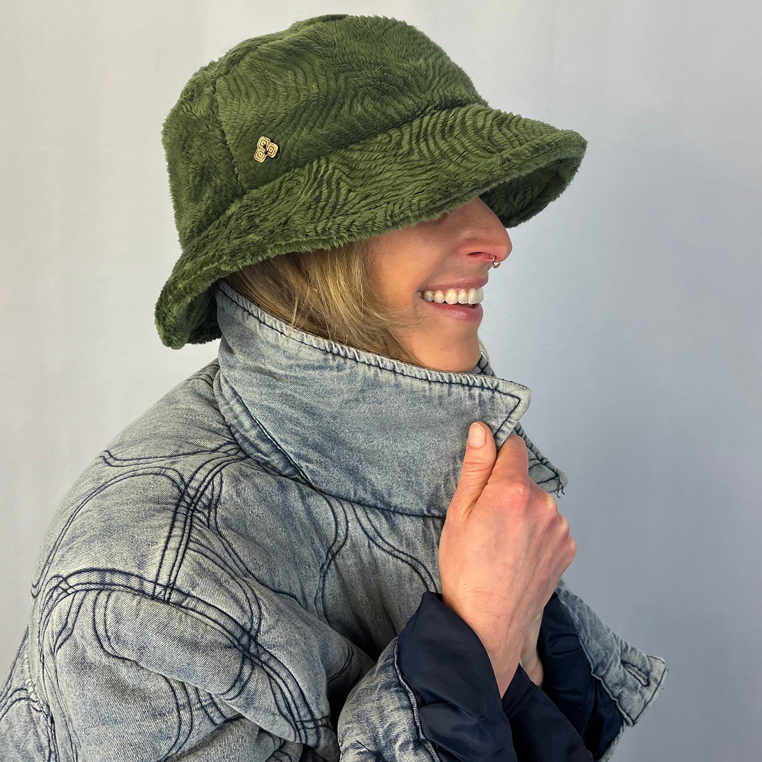 Woman side view wearing a green bucket hat and patterned jacket on a plain background