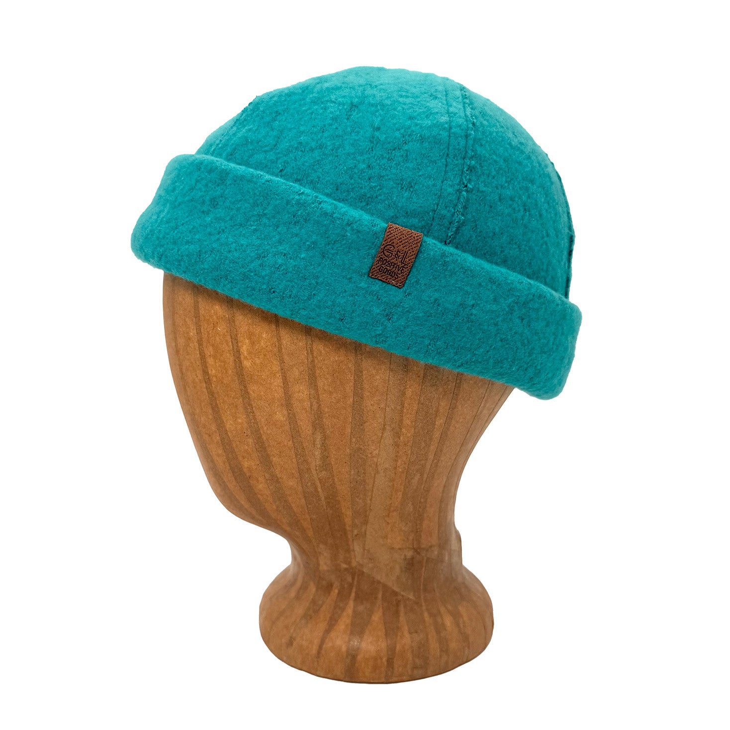 A teal blue felt knit beanie hat with a brown leather brand patch, displayed on a wooden mannequin head against a white background.