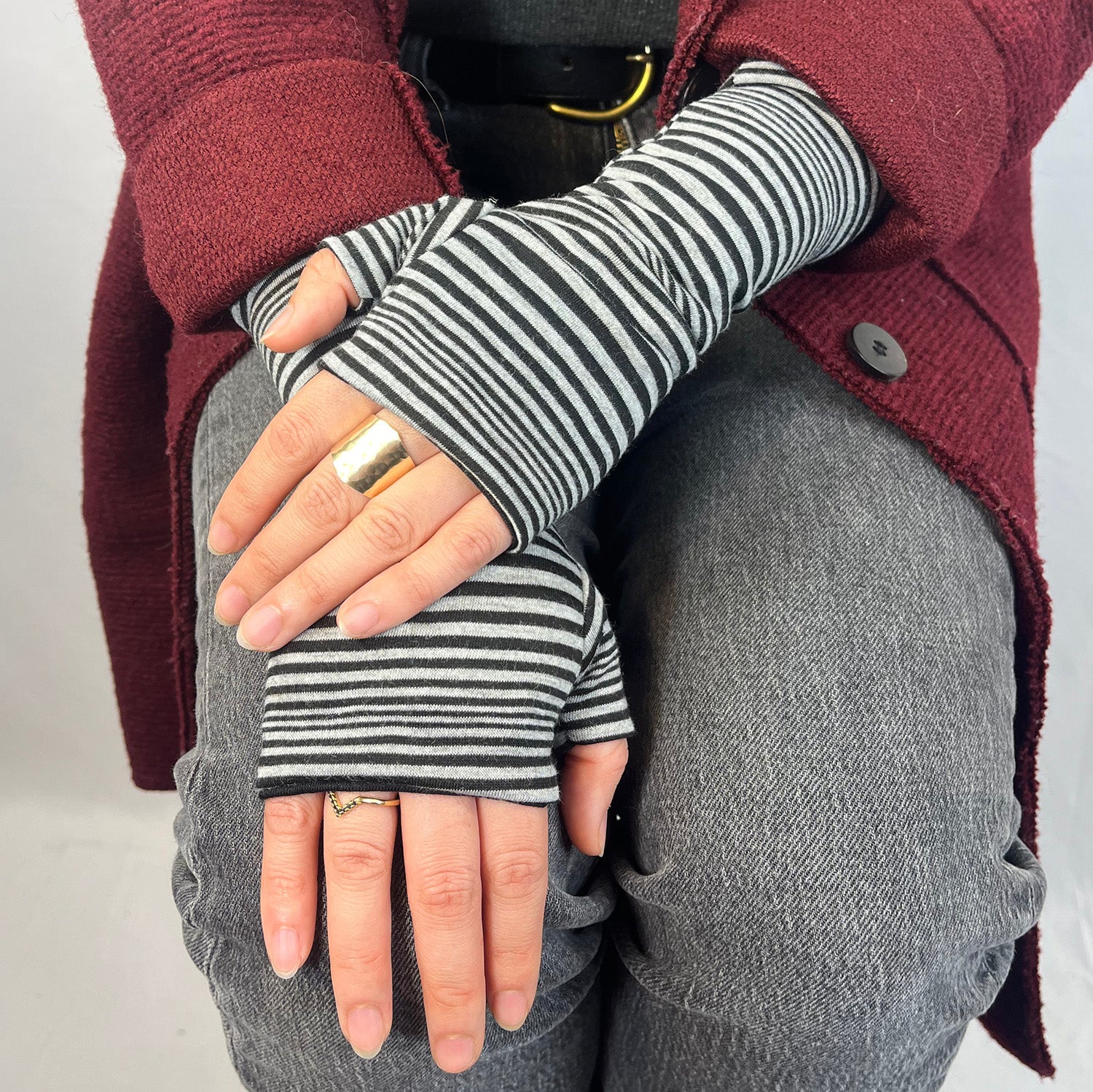 Person wearing black and grey striped fingerless gloves with a maroon jacket and gray pants.
