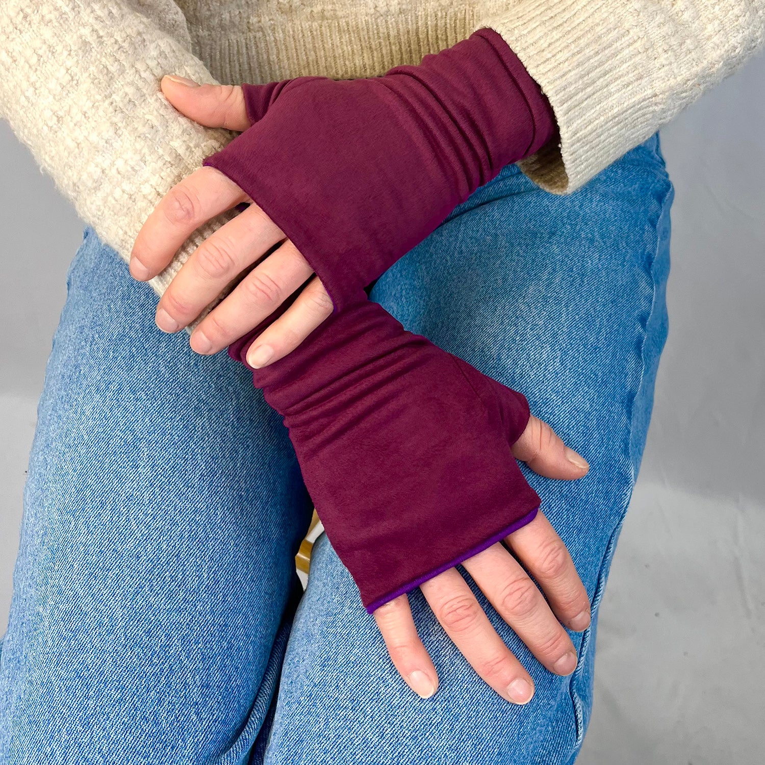 Person wearing burgundy fingerless gloves with a neutral background