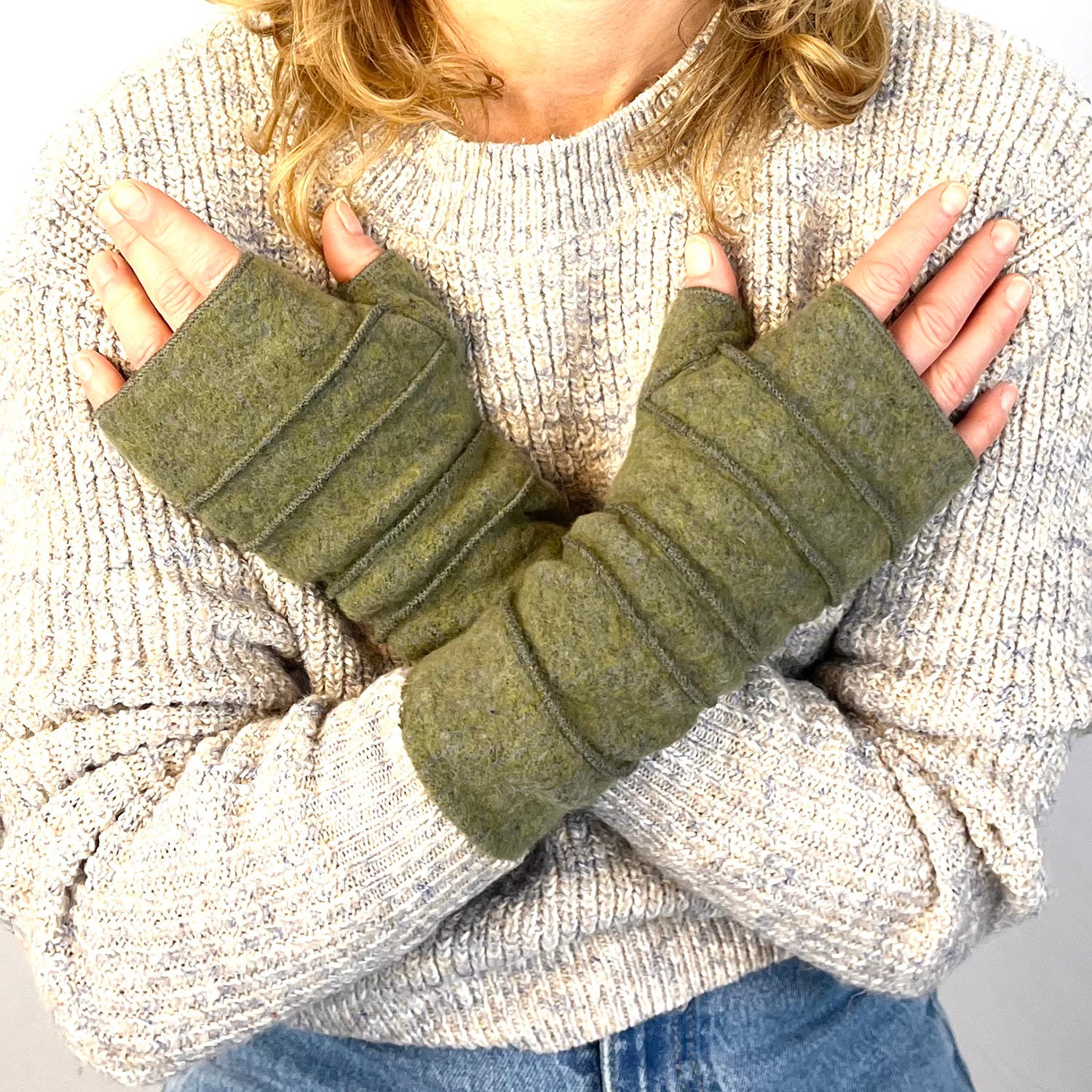 Person wearing olive green fingerless gloves with a light gray sweater and blue jeans. G & L 