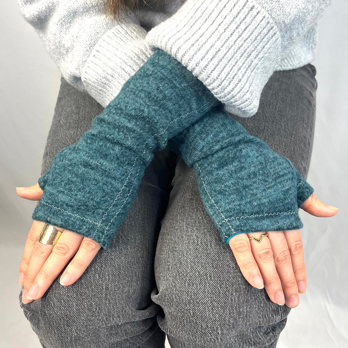 Person wearing blue fingerless gloves with a gray sweater and pants on a neutral background