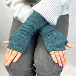 Person wearing blue fingerless gloves with a gray sweater and pants on a neutral background