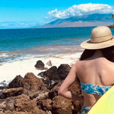 Female model wearing Hana Palm Sun Hat, showcasing the wide brim and palm straw weave on the way to surf.