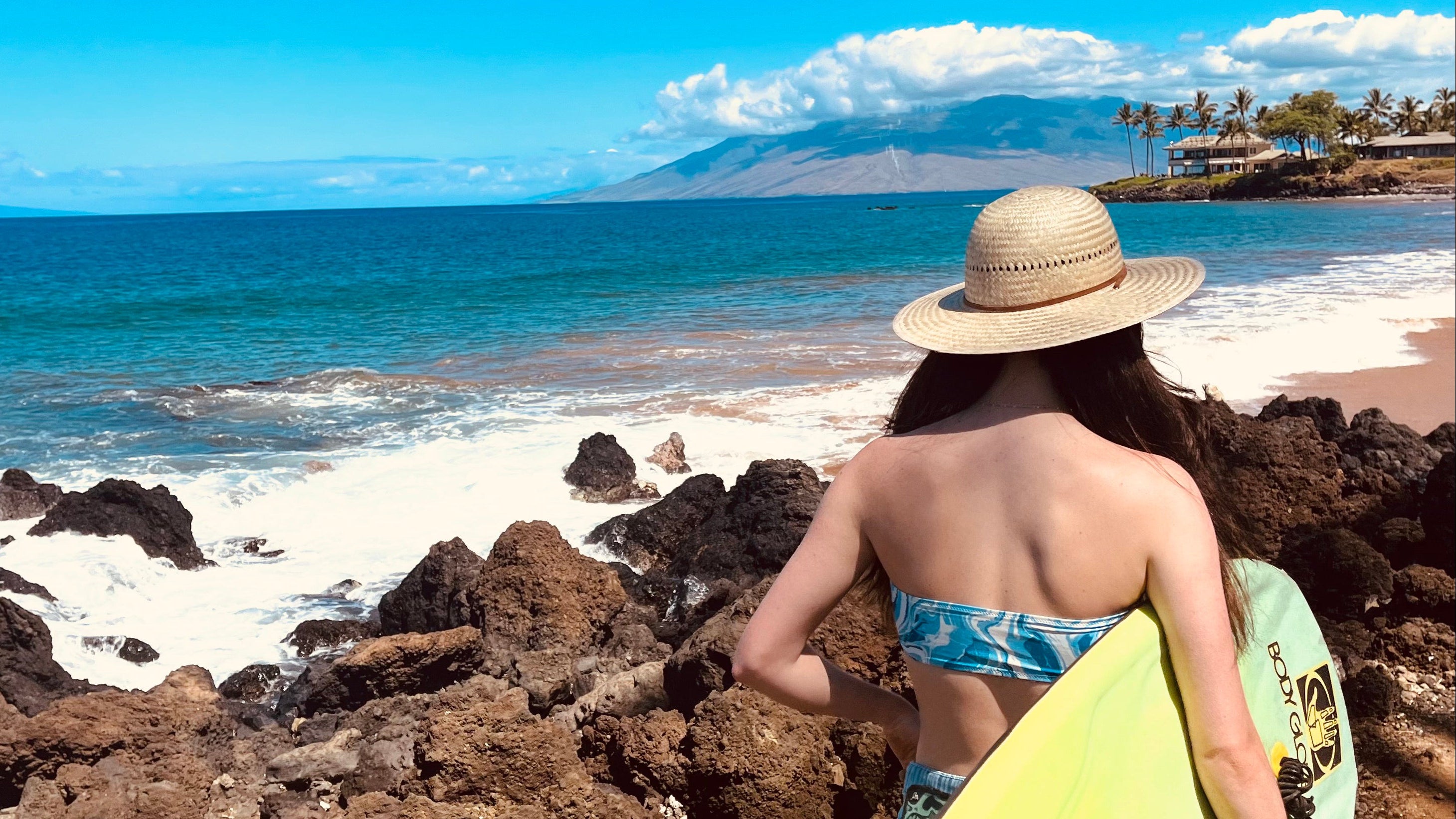 Female model wearing Hana Palm Sun Hat, showcasing the wide brim and palm straw weave on the way to surf.