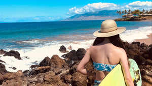 Female model wearing Hana Palm Sun Hat, showcasing the wide brim and palm straw weave on the way to surf.