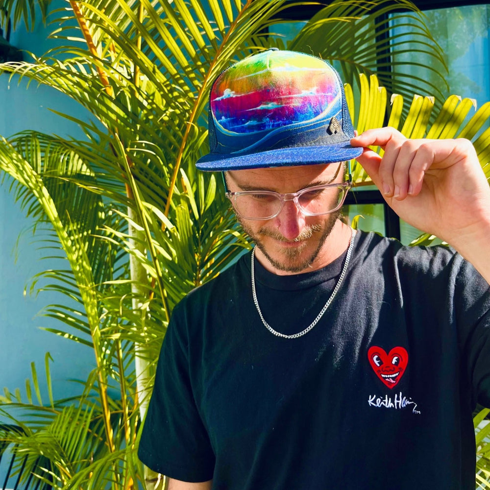 Male model styling the Horizon Rainbow Trucker Hat, featuring the bold rainbow print, mesh back, and casual look.