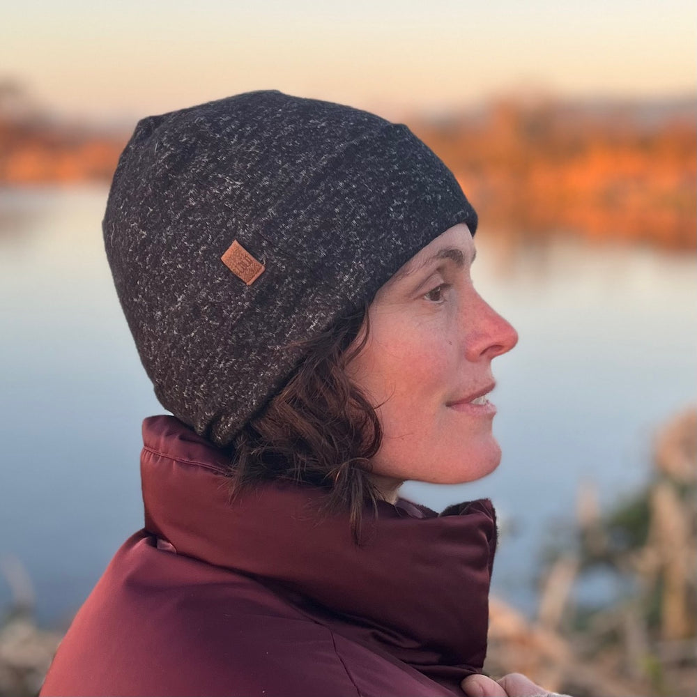 UP Beanie in Black Charcoal – worn by female model in blurred outdoor setting