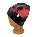 A black and red tie-dye knit beanie hat displayed on a wooden mannequin head against a white background.