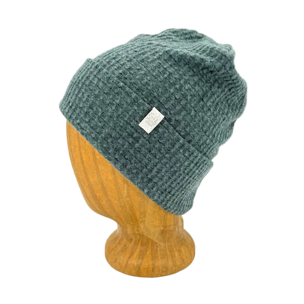 A textured knit beanie hat in a muted teal-green color, displayed on a wooden mannequin head against a white background.